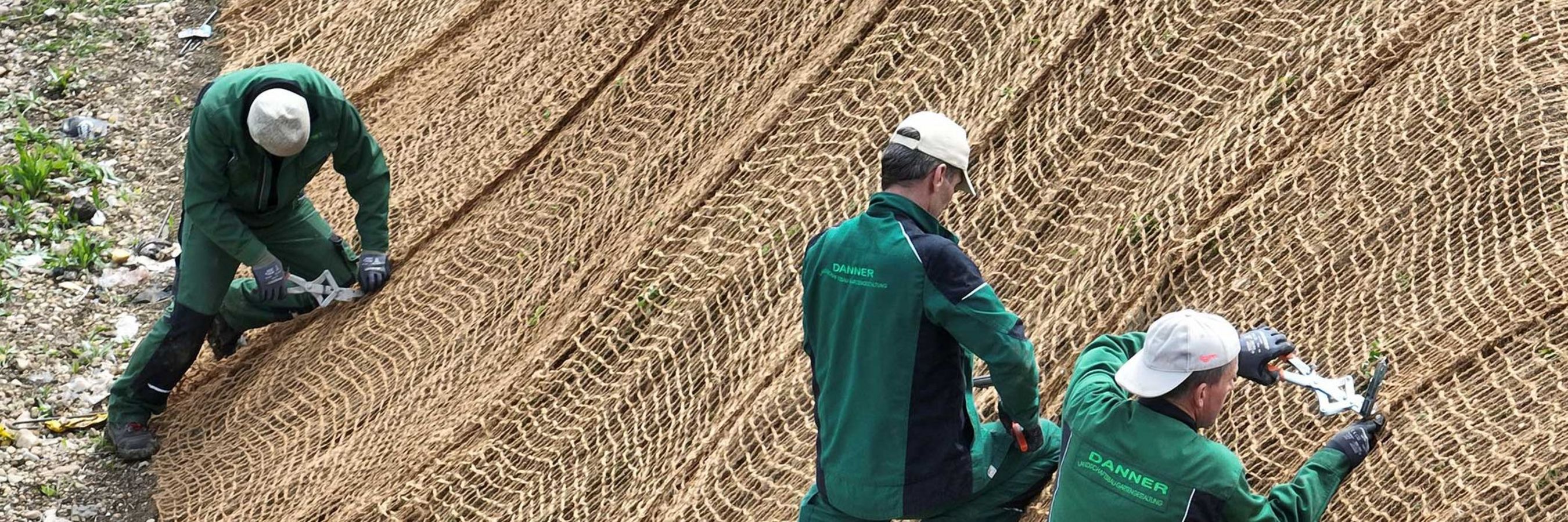 3 Arbeiter fixieren das Kokosgewebe am Hang
